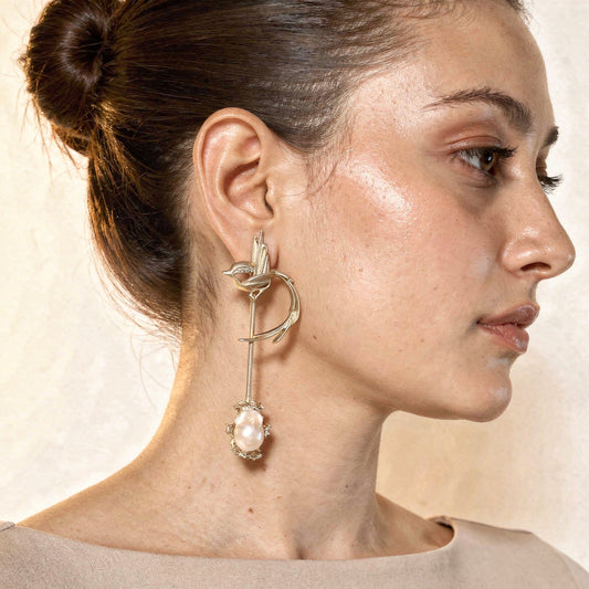 Close-up of a woman wearing an elegant earring with a pearl-like stone on a neutral background