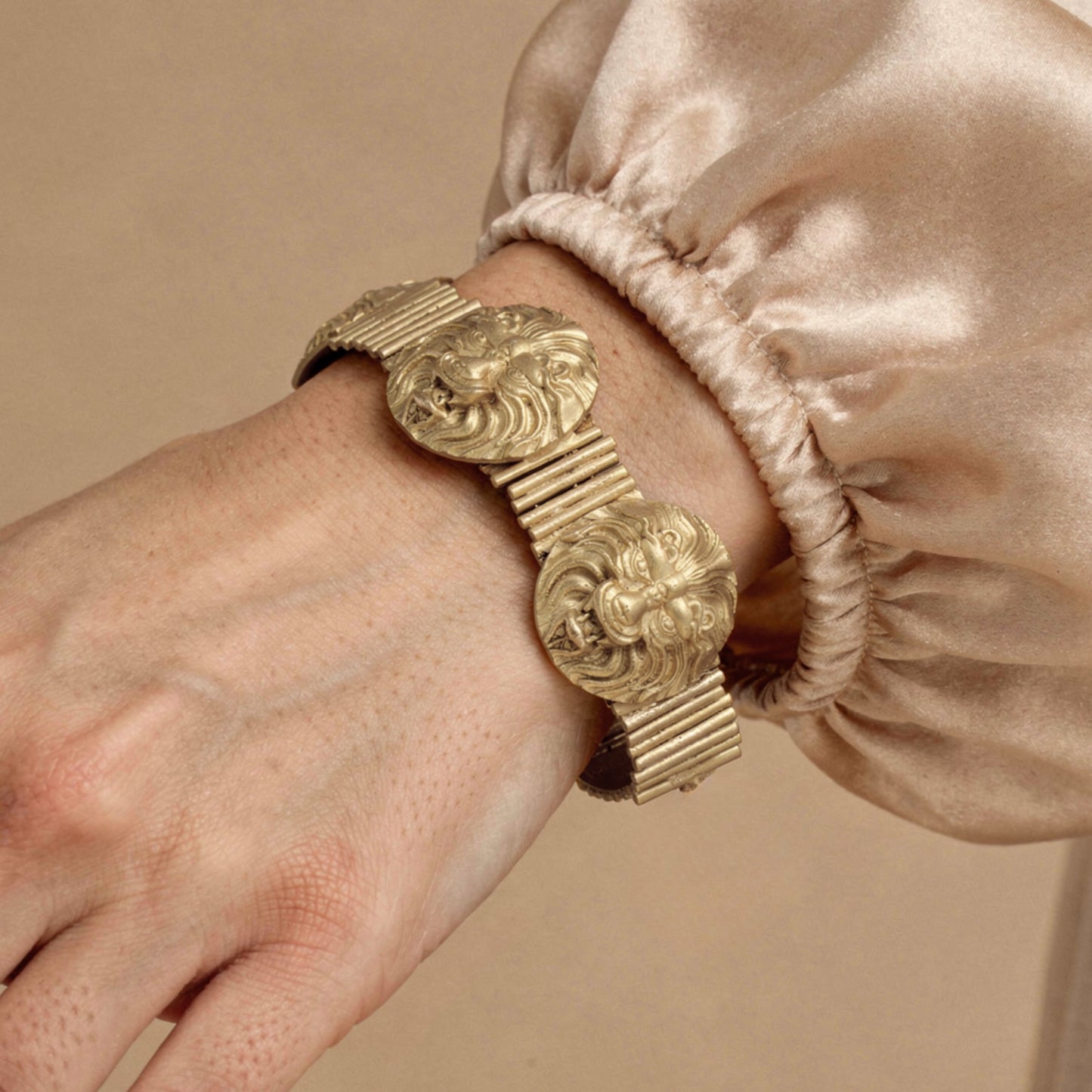 Gold bracelet with intricate design on a wrist against a beige background