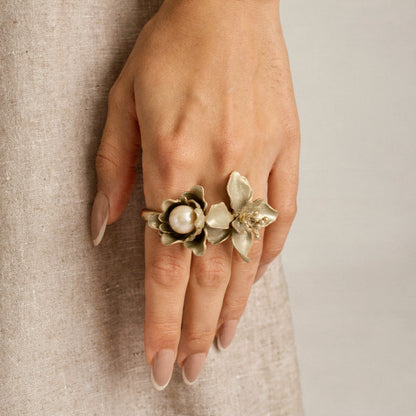Hand wearing a gold floral ring on a neutral background