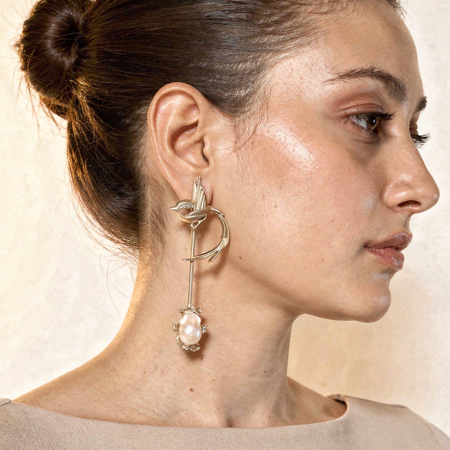 Close-up of a woman wearing an elegant earring with a pearl-like stone on a neutral background