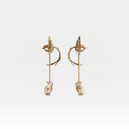 Gold earrings with pearl drops on a light gray background