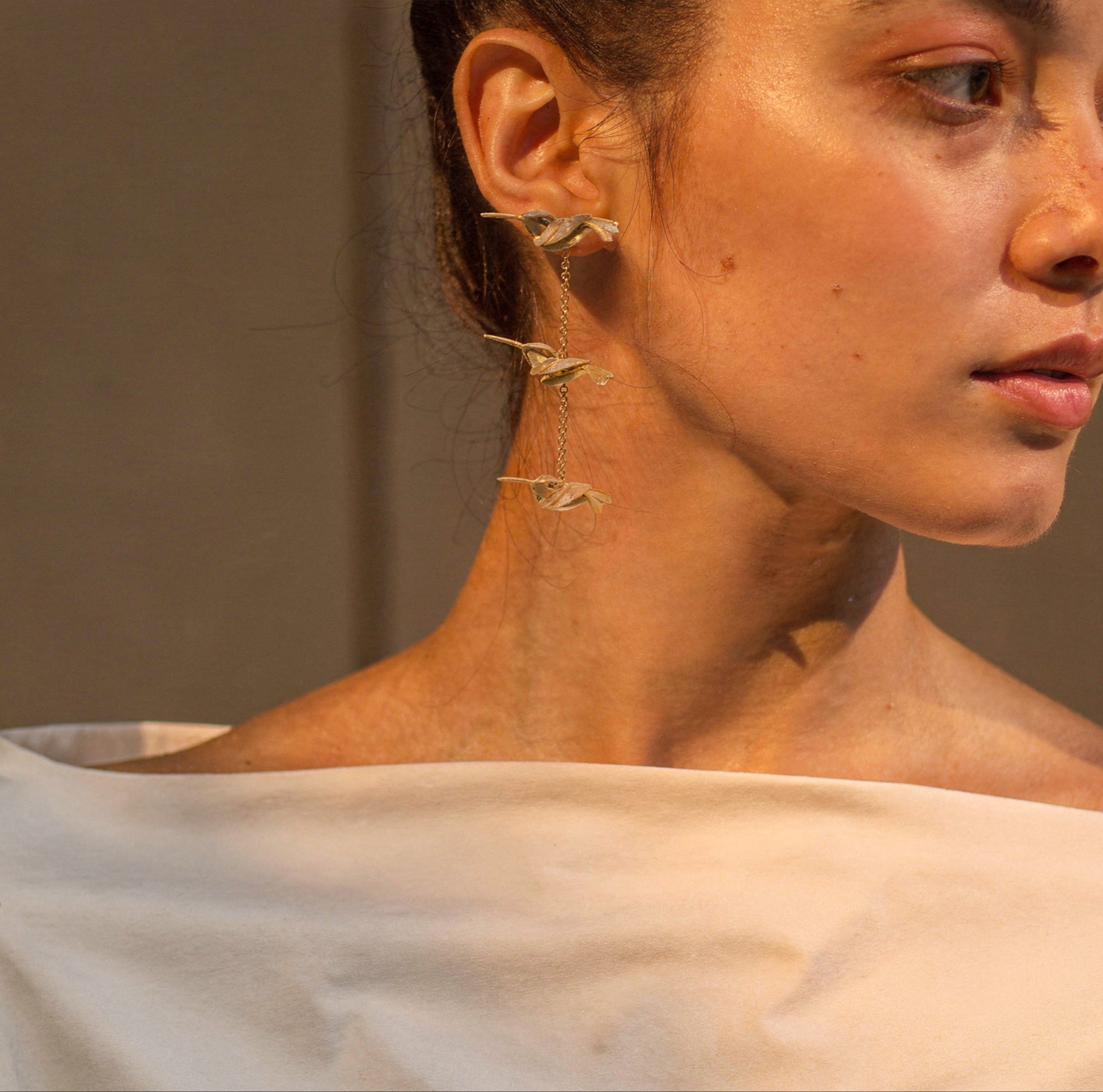 Close-up of a woman wearing gold earrings with a neutral background