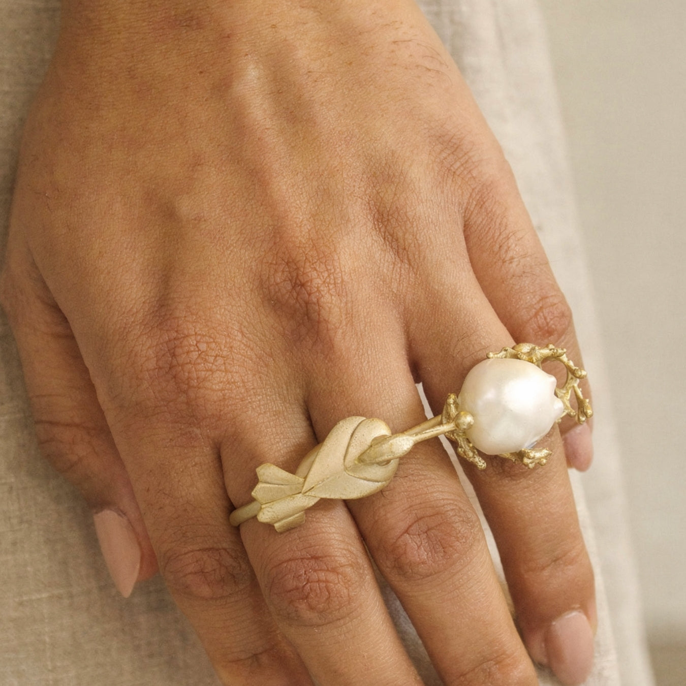Gold ring with a pearl on a person's finger against a neutral background