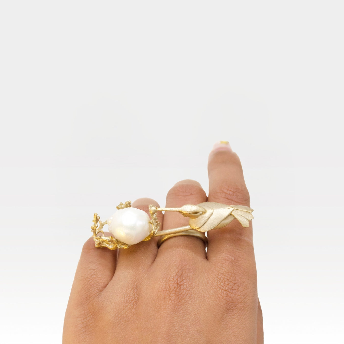 Gold ring with a pearl on a hand against a white background