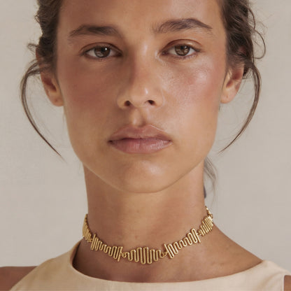 Woman wearing a gold necklace against a neutral background