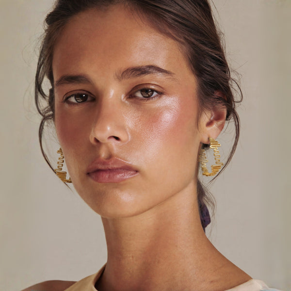 Close-up of a woman wearing gold hoop earrings against a neutral background