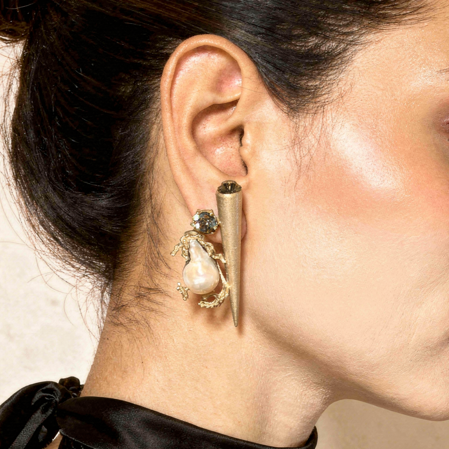 Close-up of a woman wearing an ornate earring with a pearl-like bead and gold accents.