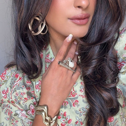 Woman wearing jewelry including earrings, ring, and bracelet with a floral patterned outfit.