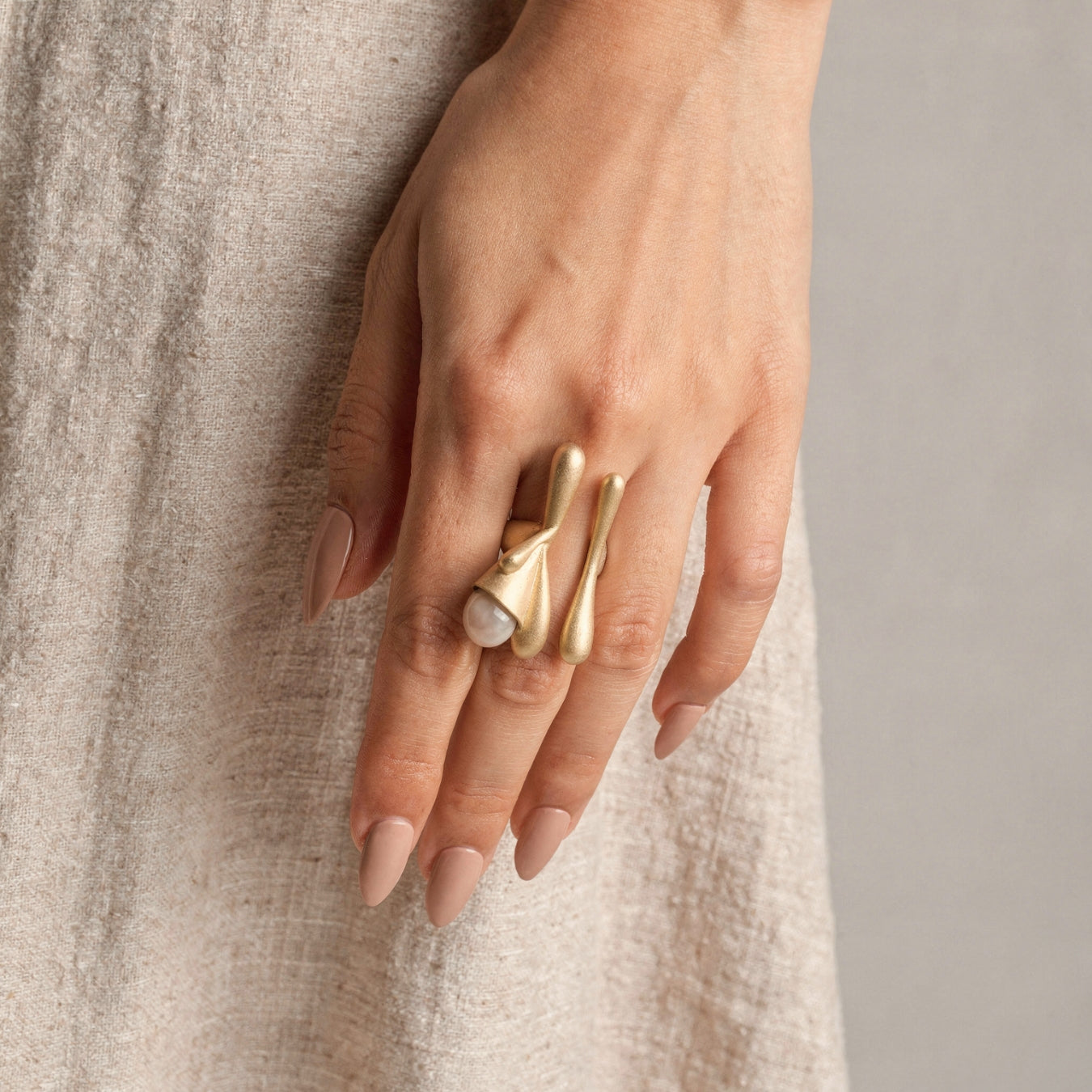 Hand wearing a gold ring with a textured beige background