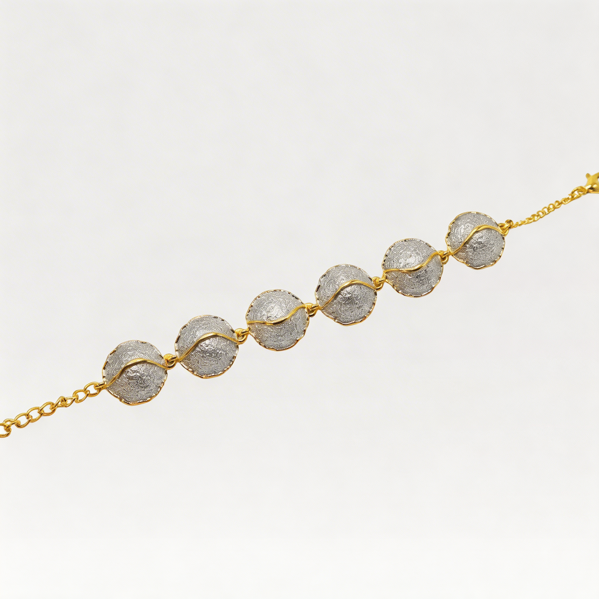 Bracelet with gold chain and metal domes on a light gray background