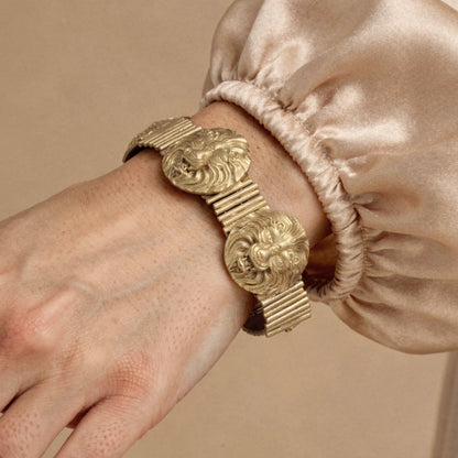Gold bracelet with intricate design on a wrist against a beige background