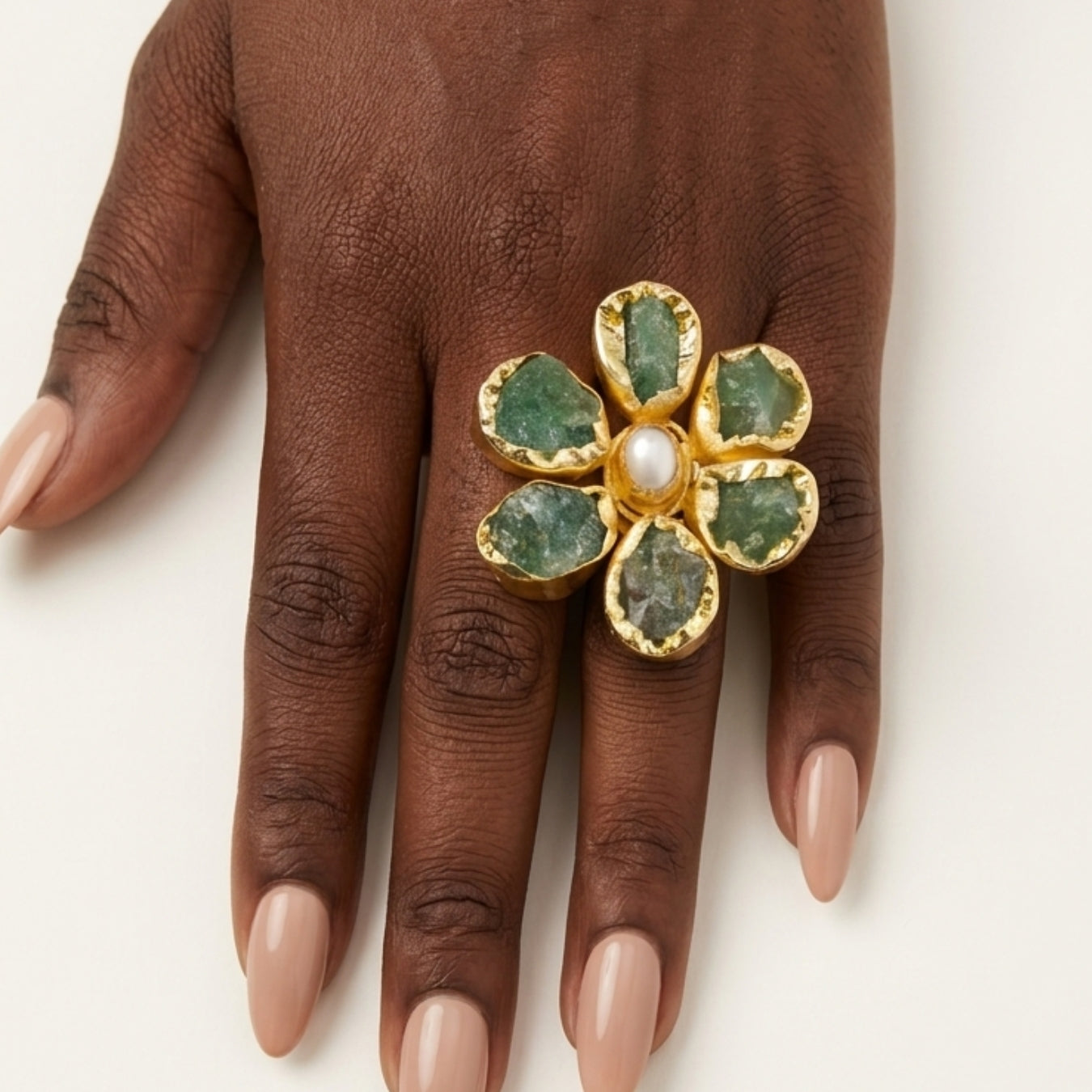Gold ring with green gemstones on a brown hand against a white background