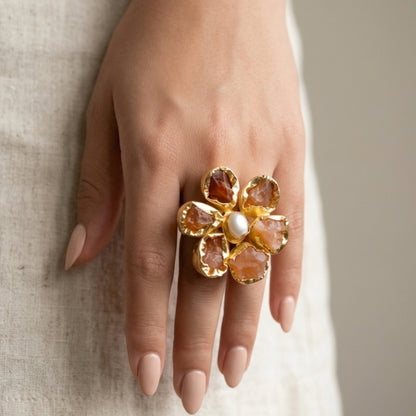 Gold flower-shaped ring with gemstones on a hand against a neutral background