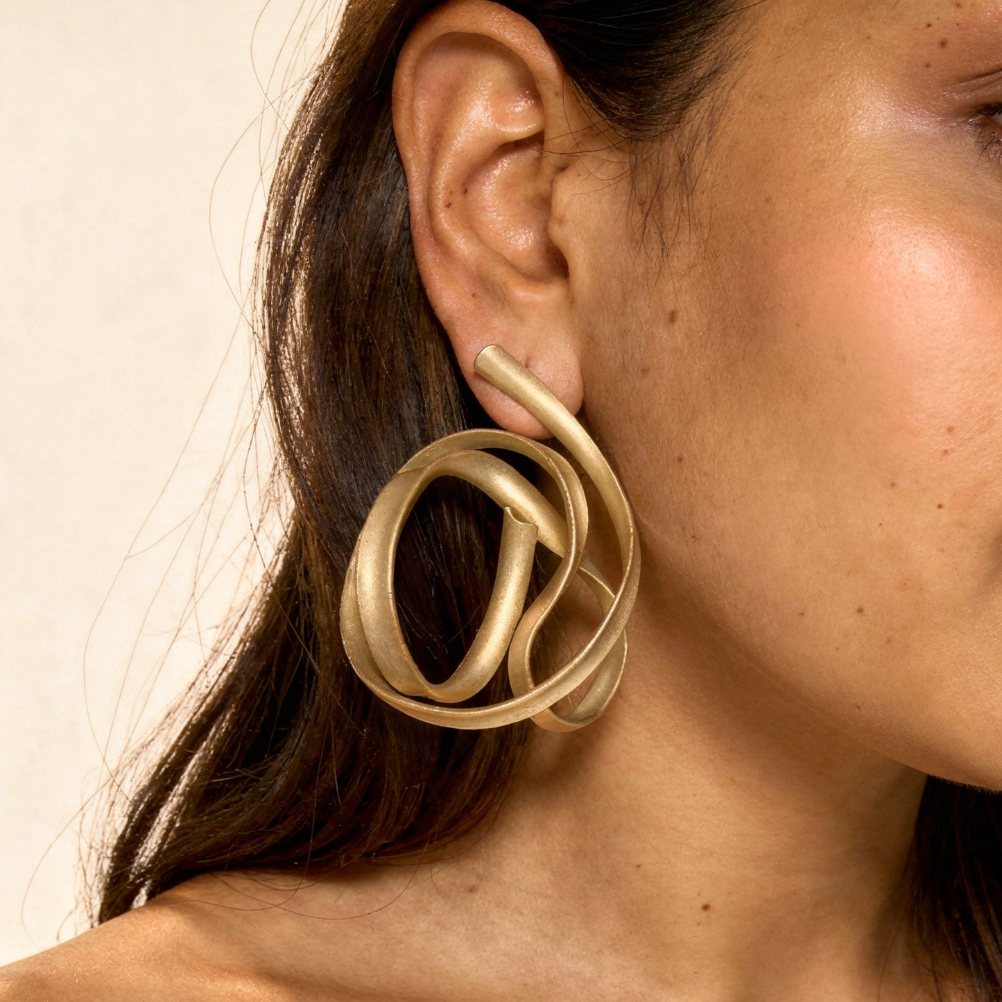 Close-up of a person wearing a gold hoop earring against a neutral background
