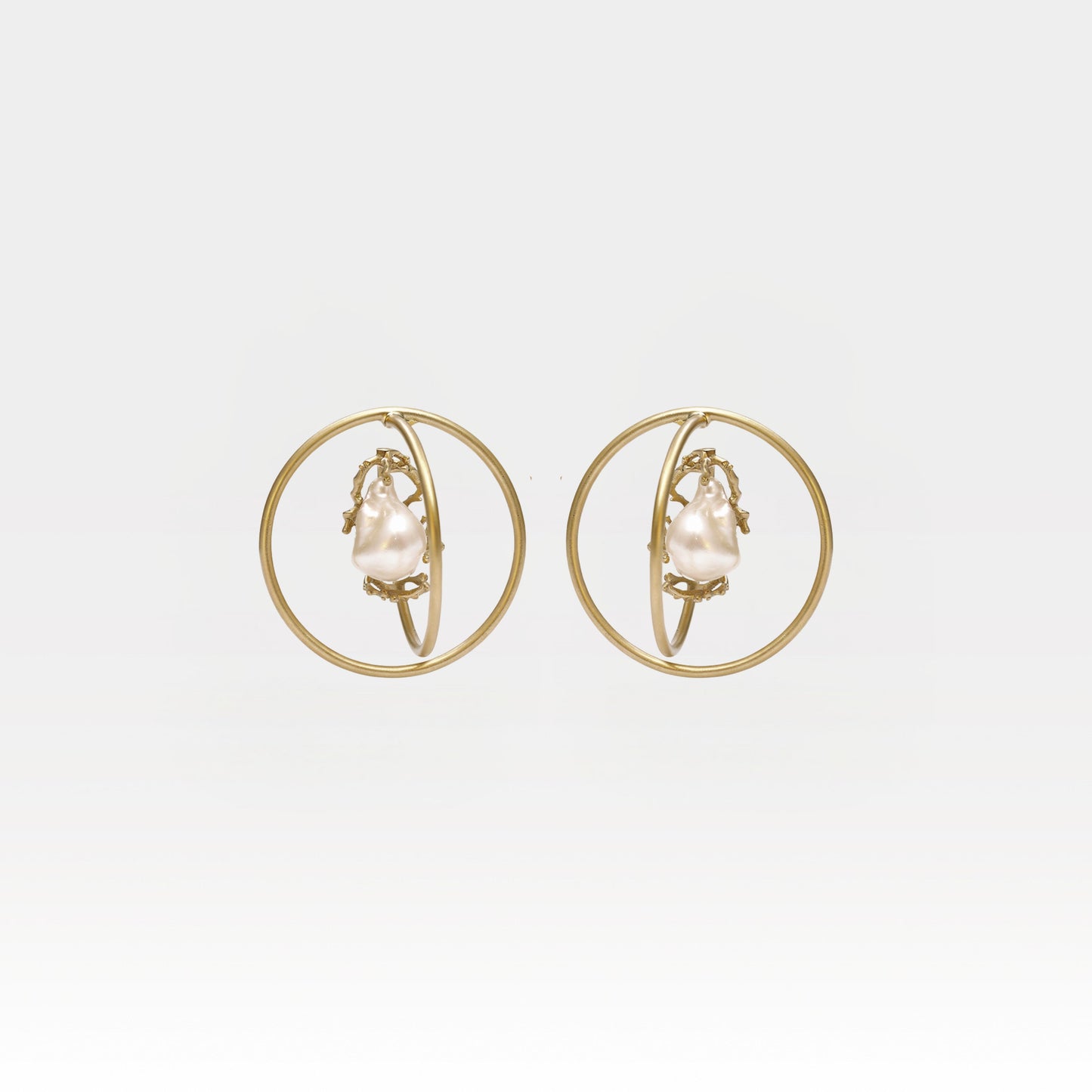 Gold hoop earrings with pearl center on a light gray background