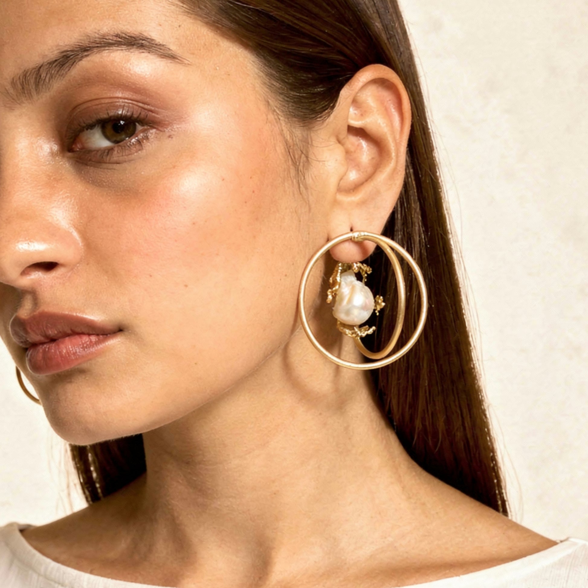 Close-up of a woman wearing gold hoop earrings with a pearl center.