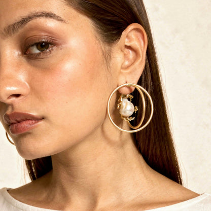 Close-up of a woman wearing gold hoop earrings with a pearl center.