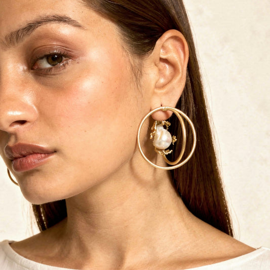Close-up of a woman wearing gold hoop earrings with a pearl center.
